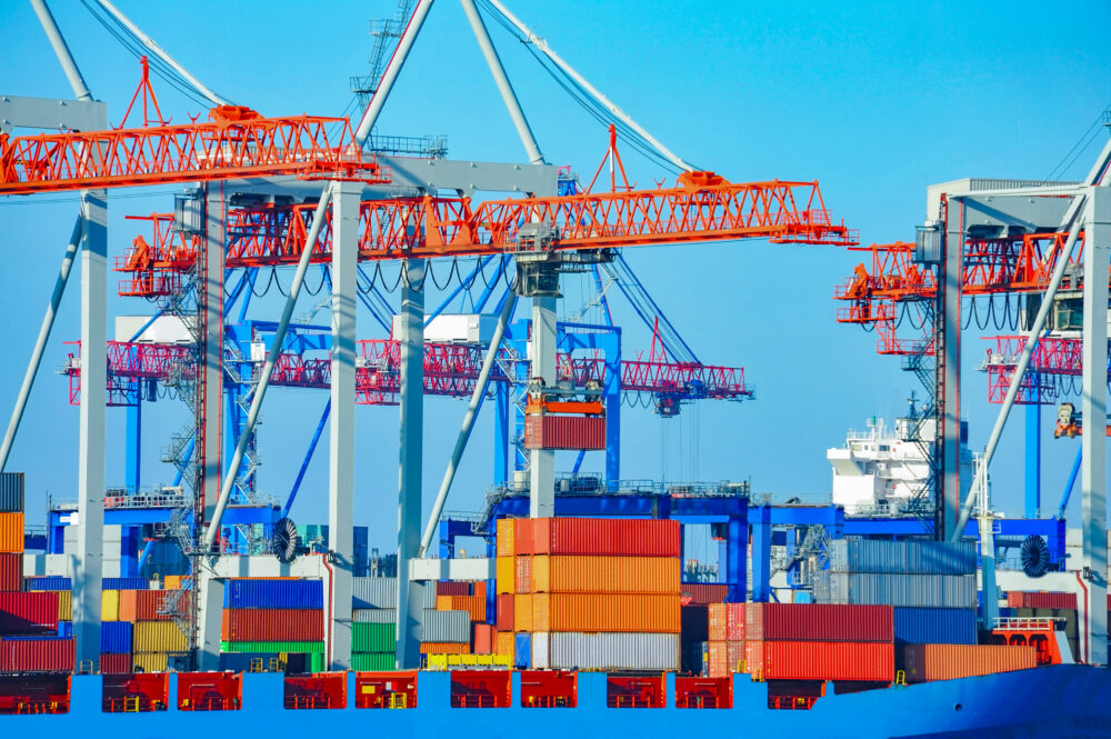 Ocean freight port terminal with cranes and stacked containers.